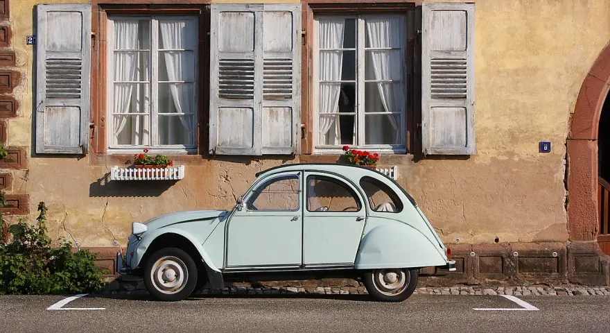 Jasnoniebieski, zabytkowy Citroen 2CV, jeden z klasycznych modele stare, parkuje przed kamiennym domem z drewnianymi okiennicami.