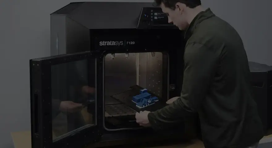 Mężczyzna wkłada wydrukowany model do drukarki 3D Stratasys F120. Tak wygląda drukarka 3d w akcji.