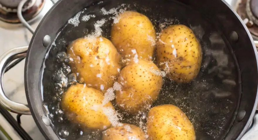 Mehrere ganze Kartoffeln kochen in einem Topf mit sprudelndem Wasser auf dem Herd.