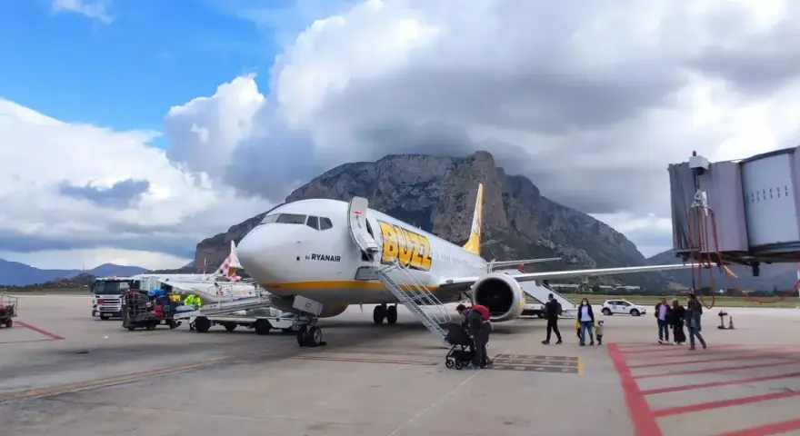 Samolot Buzz by Ryanair na lotnisku na Sycylii, z górami w tle.