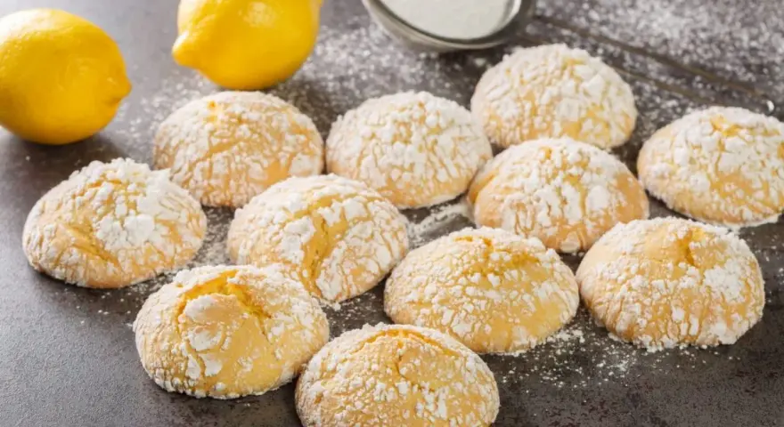Deliziosi biscotti al limone spolverati di zucchero a velo, con limoni freschi sullo sfondo.