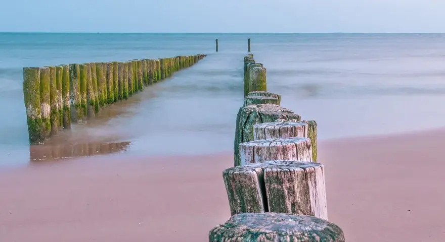 Drewniane pale tworzą ścieżkę wzdłuż plaży, prowadzącą w stronę morza. To idealne miejsce na spacer, odkrywając kąty rybackie trasę.