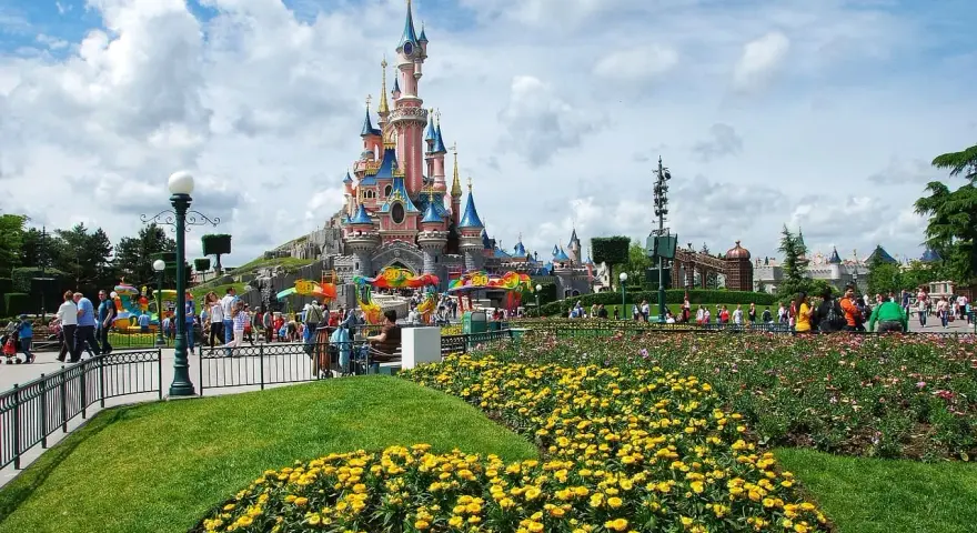Disneyland Paris castle with colorful flowers and crowds of people.