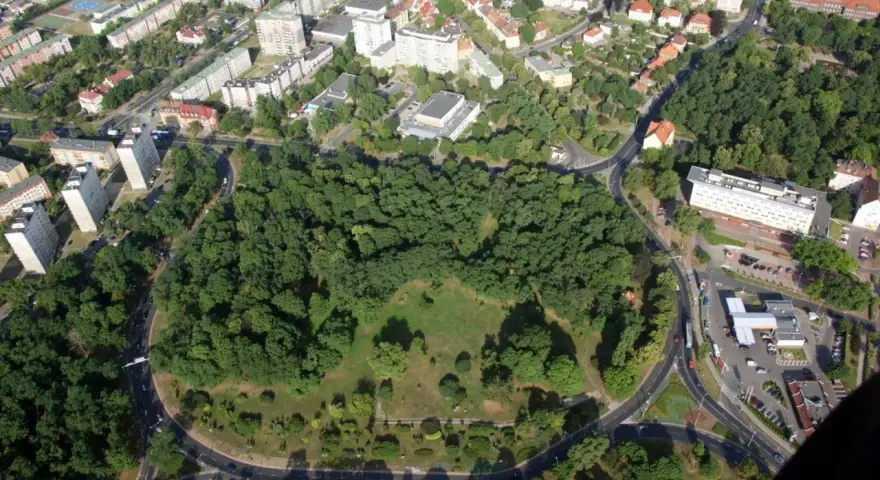 Widok z lotu ptaka na zielony park otoczony drogami, z budynkami mieszkalnymi w tle. To największe rondo w Polsce, które otacza serce miasta.