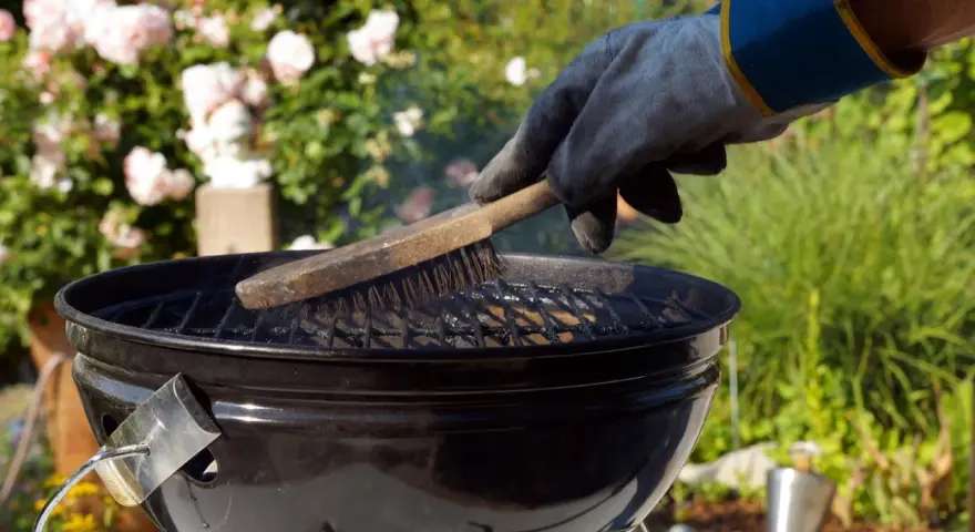Mit einem Handschuh wird der Grillrost gereinigt. Rauch steigt auf, während die Bürste über die Roste fährt.