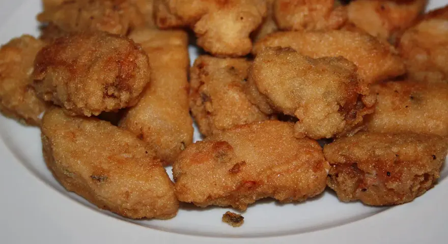 Un plato blanco lleno de trozos dorados y crujientes de japuta en adobo, listos para disfrutar.