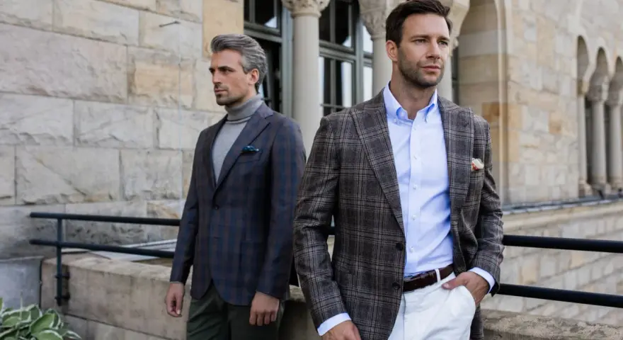 Dwóch eleganckich mężczyzn w marynarkach w kratę. Jeden ma szary golf, drugi błękitną koszulę. Stylowy mankiet co to?
