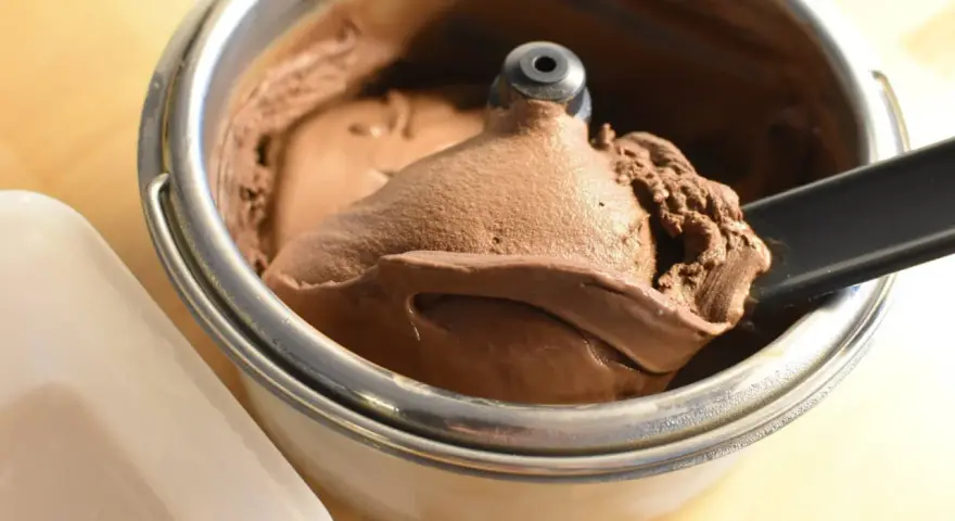 Un cucchiaio nero preleva una porzione di cremoso gelato fatto in casa al cioccolato da una gelatiera.
