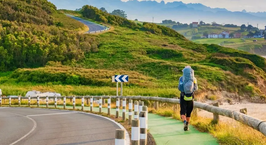 Pielgrzym z plecakiem idzie ścieżką wzdłuż wybrzeża, jedną z wielu tras Camino de Santiago.