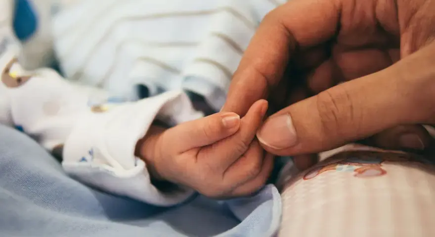 Dłoń rodzica obejmuje maleńką dłoń dziecka. To symbol miłości i troski, a także przygotowań do złożenia wniosku o urlop macierzyński.