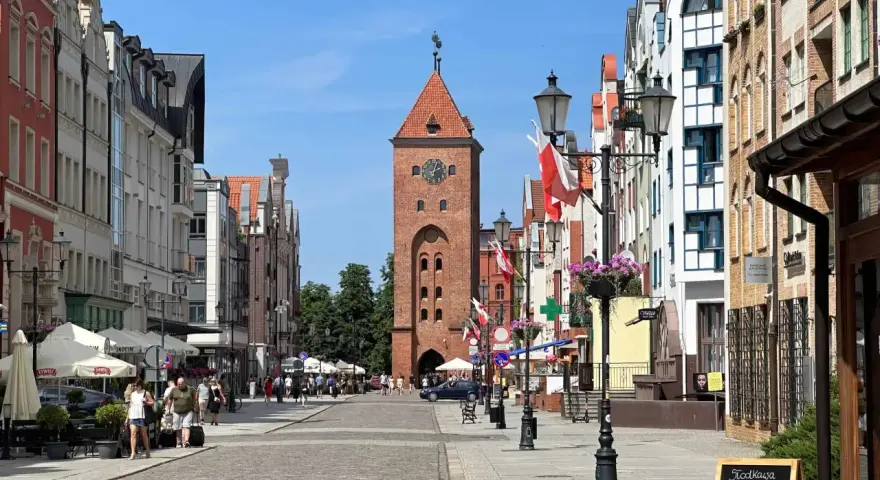 Ulica w Elblągu, z charakterystyczną wieżą i kolorowymi kamienicami. To najniżej położone miasto w Polsce, pełne urokliwych zakątków.