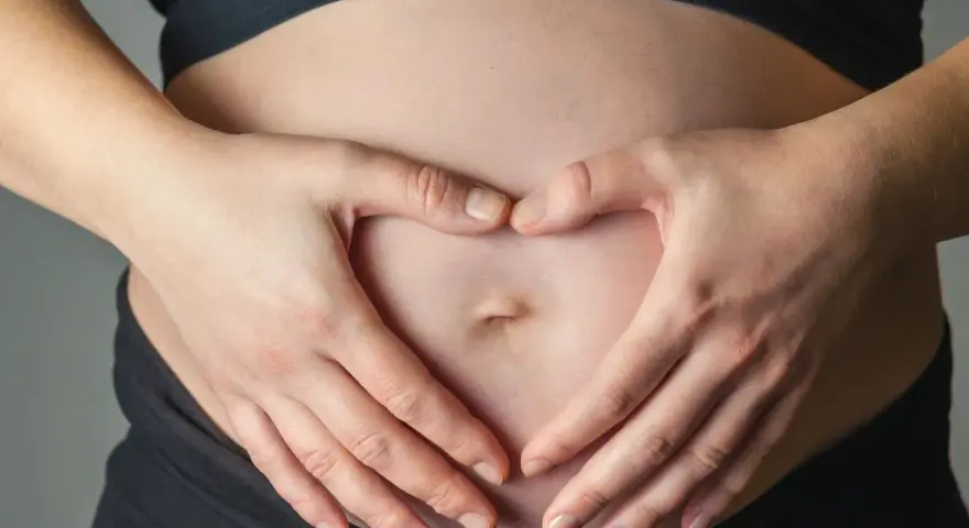 Dłonie tworzą serce na brzuchu, symbolizując miłość i troskę o to, jak dziecko oddycha w brzuchu.