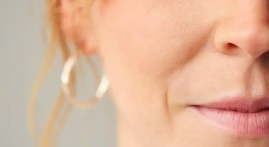 Nahaufnahme eines Gesichts mit sichtbarer Nasolabialfalte, die mit 40 Jahren typisch ist. Eine Frau mit dezentem Lächeln.