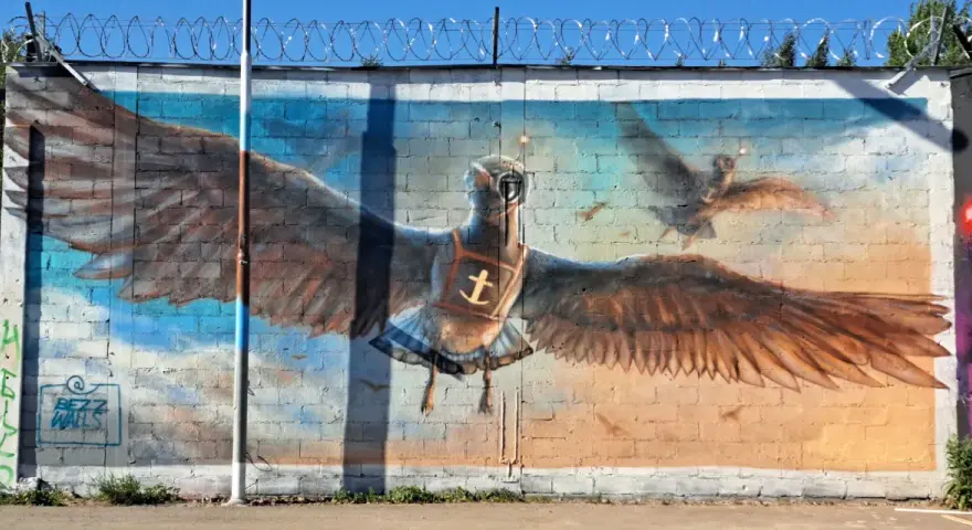 Street art i Stockholm: en stor målad fågel med utbredda vingar, som flyger mot en blå himmel.