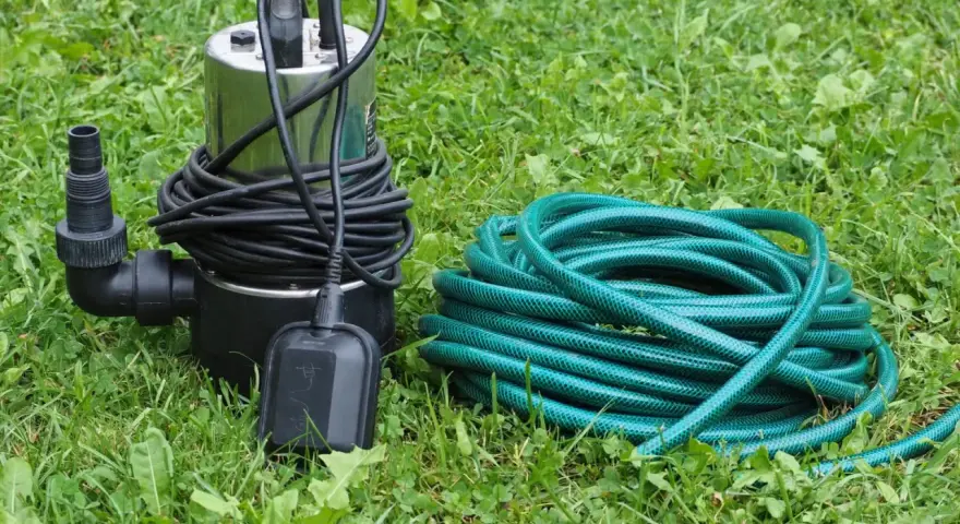 Pompa do podlewania ogrodu i zielony wąż ogrodowy leżą na trawie. Idealny zestaw do nawadniania.