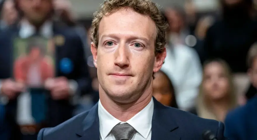 Mark Zuckerberg im Anzug, im Hintergrund unscharfe Menschen und ein Foto.