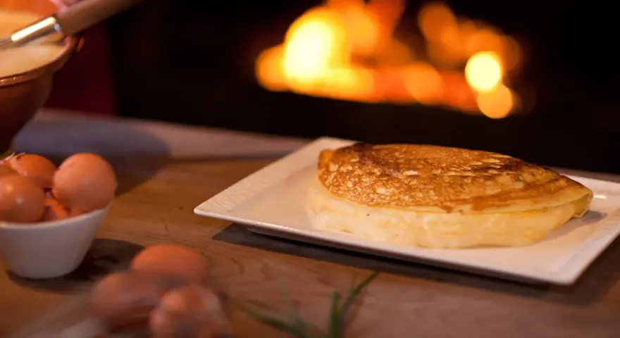 Une omelette mere poulard dorée et moelleuse, prête à être dégustée près d'un feu de cheminée. Des œufs frais sont visibles à côté.