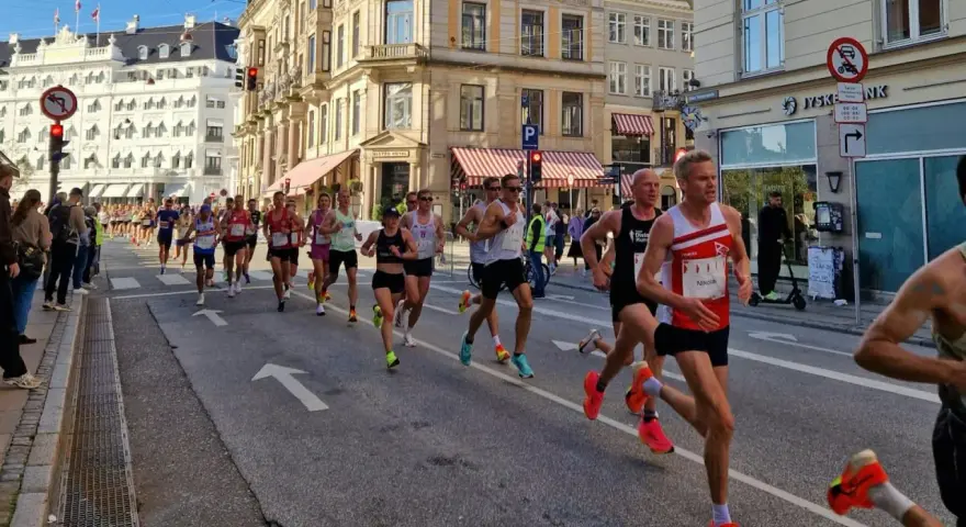 Corredores compiten en una media maratón en Europa, con edificios históricos y público animando.
