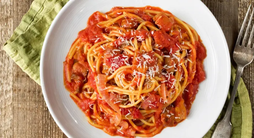 Spaghetti al pomodoro con pezzi di carne e cipolla, uno dei classici sughi per pasta, spolverati di parmigiano.