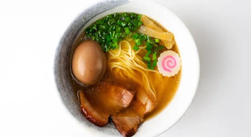 A miseczce shoyu ramen z makaronem, jajkiem, plastrami wieprzowiny, szczypiorkiem, bambusem i różową rybną kluską.