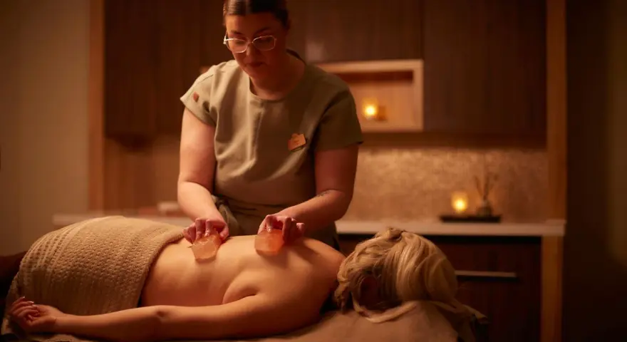 A therapist performs a Himalayan salt massage, placing warm salt stones on a client's back.