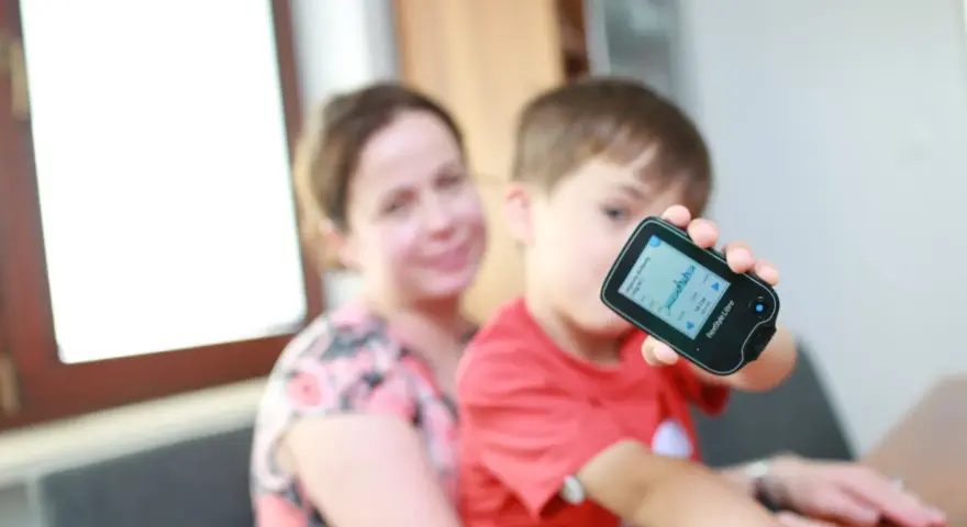 Chłopiec z mamą monitoruje poziom glukozy, co może być związane z objawami cukrzycy u dzieci.