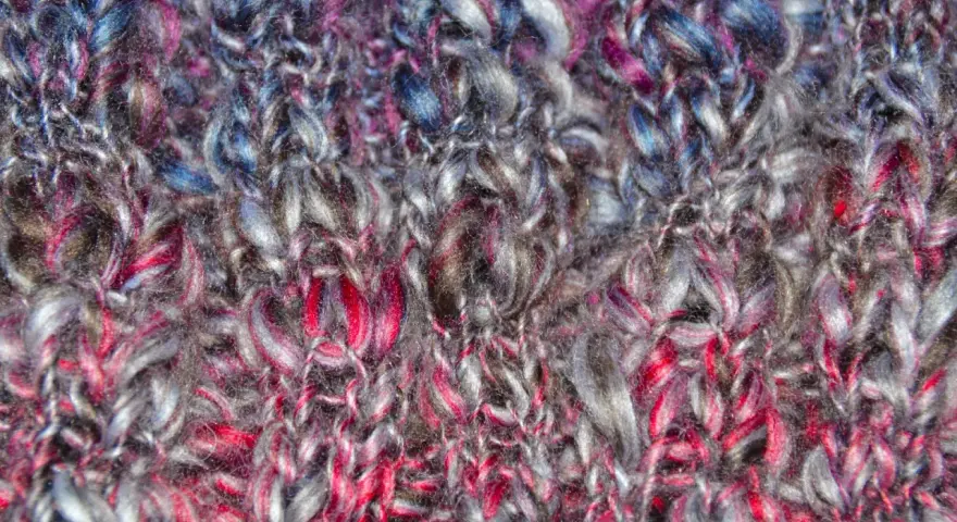 Detaljerad vy av en stickad tubhalsduk i garn med färger som grått, rosa och blått. Mönstret är en enkel slätstickning.