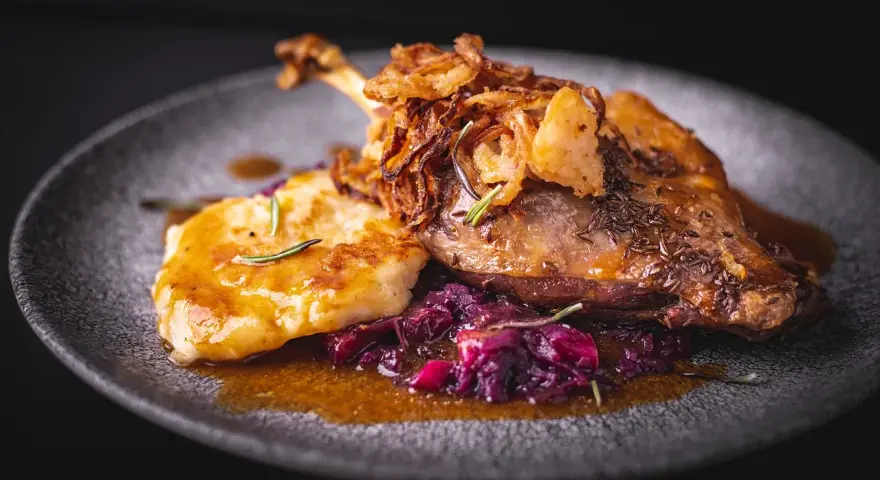 Pieczona kaczka z chrupiącą cebulką, purée i czerwoną kapustą na talerzu.