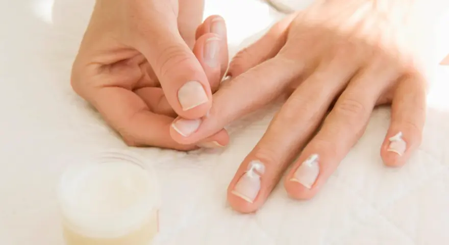 Application de crème pour hydrater la peau sèche autour des ongles.