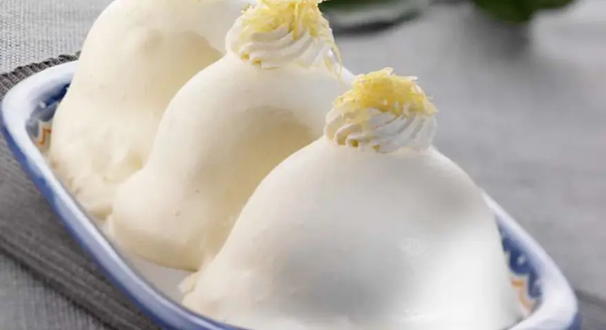 Tre deliziose delizie al limone, guarnite con panna e scorza di limone, in un piatto blu e bianco.