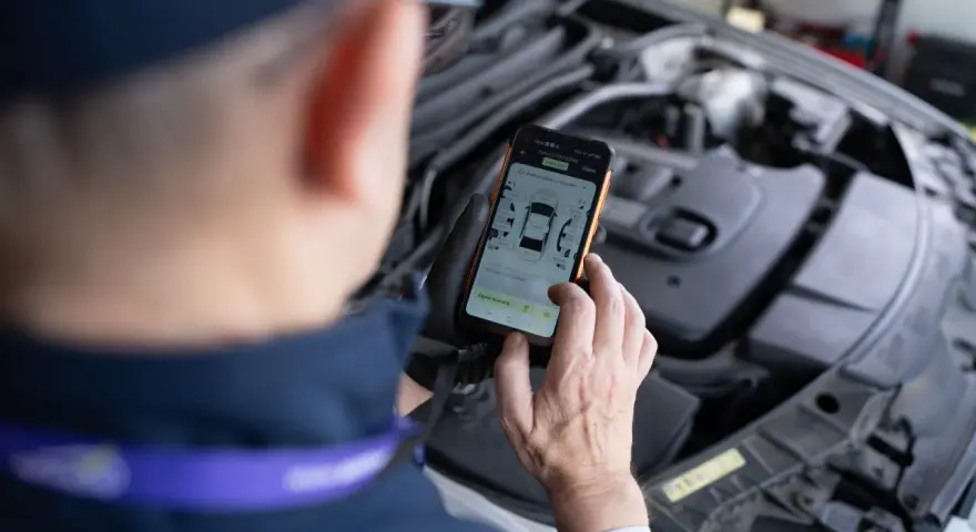 Mechanik sprawdza kody błędów DTC Renault na telefonie, analizując raport z pomiaru lakieru.