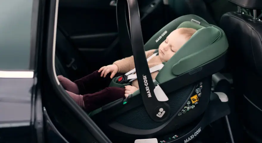 Schlafendes Baby in einer grünen Babyschale mit Isofix-Autobefestigung. Sicher und bequem auf Reisen.