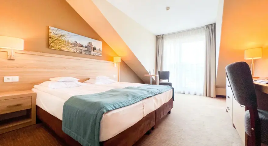 Przytulny pokój hotelowy z wygodnym łóżkiem, biurkiem i oknem. Idealne miejsce na nocleg tranzytowy, by odpocząć w podróży.