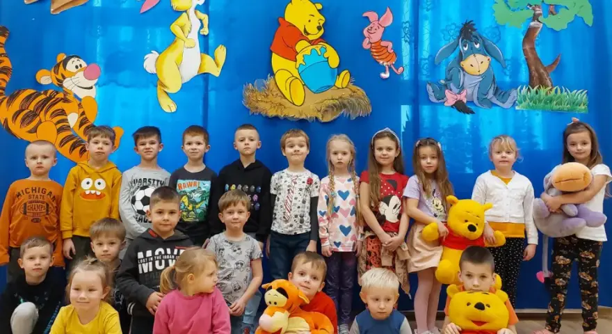 Dzieci pozują do zdjęcia z Kubusiem Puchatkiem i przyjaciółmi, świętując Dzień Kubusia Puchatka.