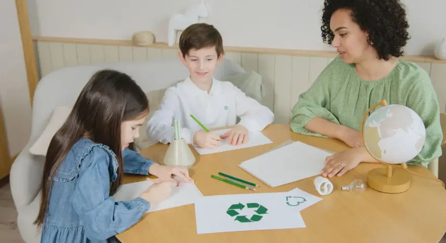 Dzieci i nauczycielka tworzą scenariusz zajęć "z ekologią na ty". Na stole symbol recyklingu, żarówki i globus.