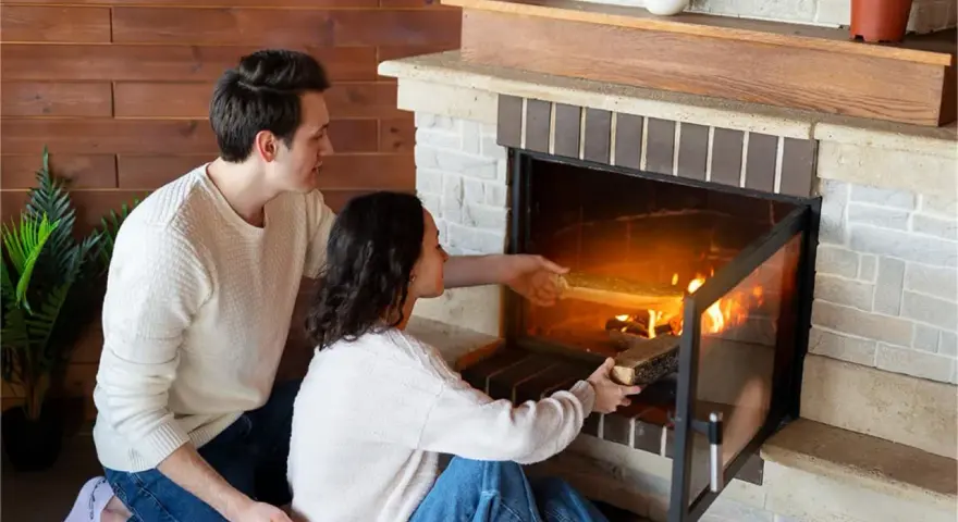 Pareja añade leña a la chimenea, creando un ambiente acogedor. Los insertables de madera se queman, iluminando la habitación.