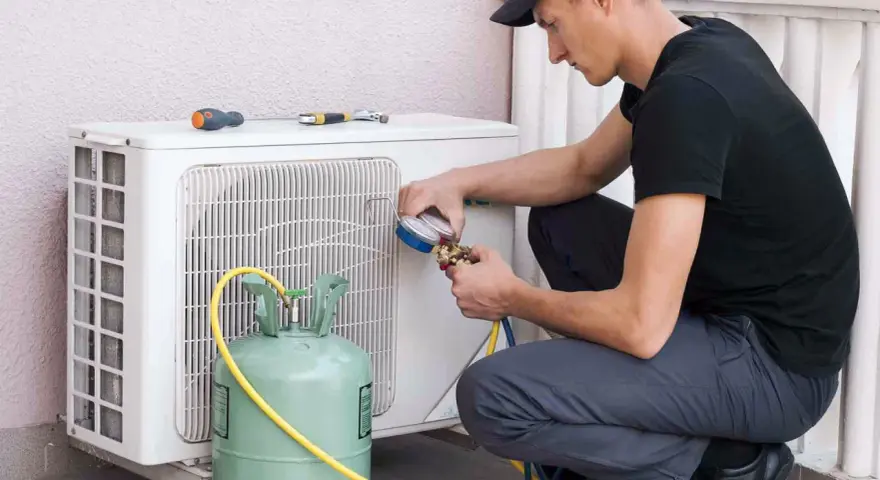 Técnico recargando gas aire acondicionado casa. Manómetro y tanque verde conectados a la unidad exterior.