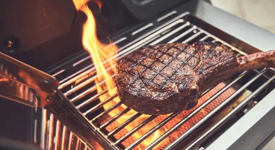 Ein saftiges Steak wird auf einem Gasgrill gegrillt, Flammen züngeln empor.