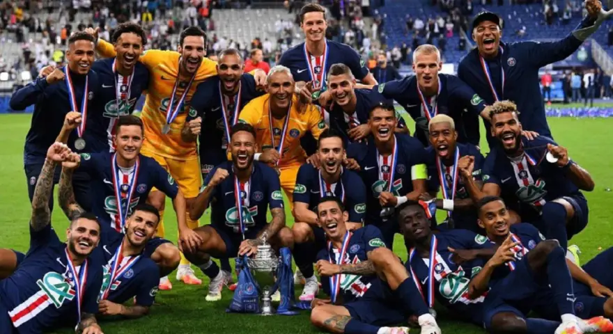 Un grupo de jugadores de Ligue 1 celebra con trofeos y medallas, sonriendo y vitoreando en el campo.