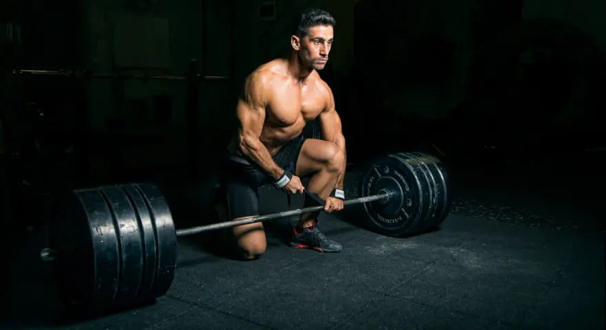 Un homme musclé s'apprête à soulever une barre chargée, profitant d'un temps de repos musculation dans une salle sombre.