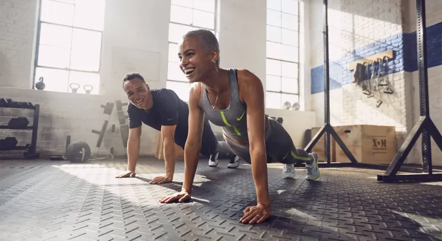 Coppia sorridente in palestra, che fa flessioni. Lo sport è un valido alleato contro la depressione, un modo per ritrovare energia e benessere.