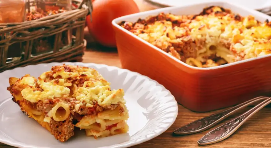 Zapiekanka makaronowa z mięsem mielonym w sosie śmietanowym, podana na talerzu i w naczyniu żaroodpornym.