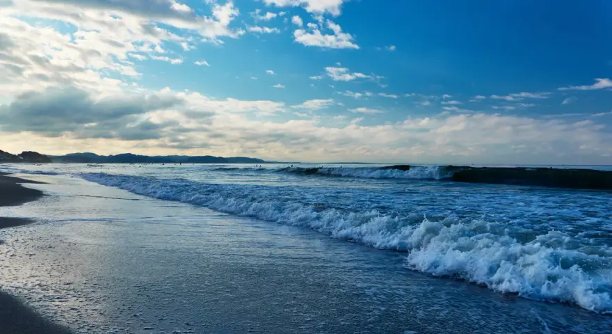 Plaża nad Bałtykiem z falami i błękitnym niebem z chmurami.