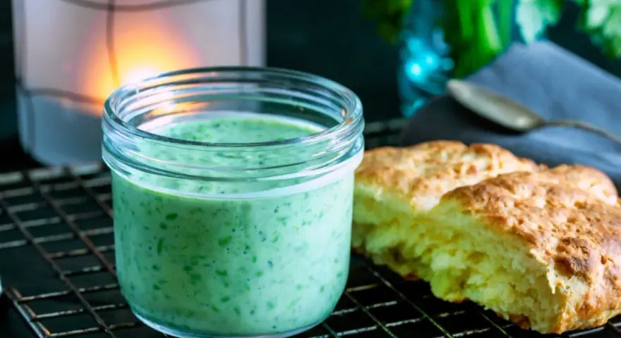 En burk med krämig, grön dressing, perfekt för ett grönt gudinnedressing recept. Bredvid ligger nybakade scones.