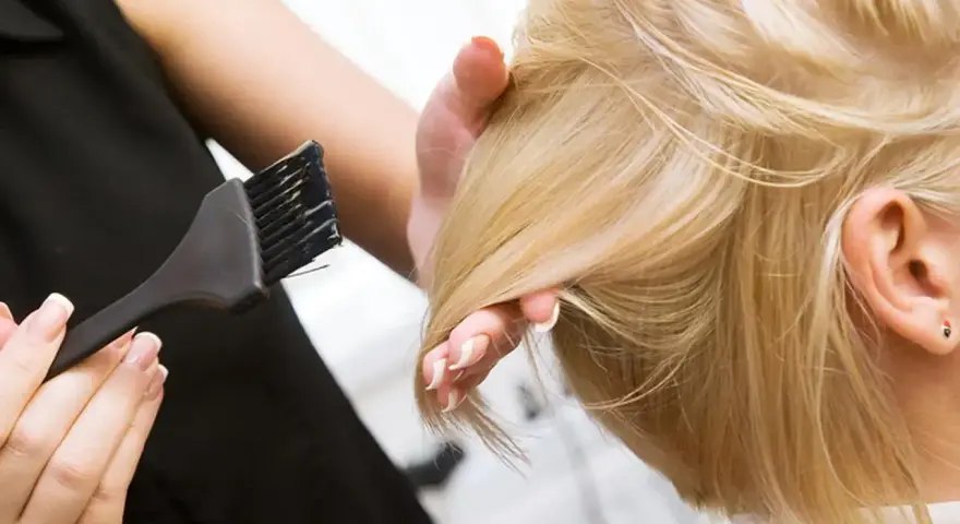 Fryzjerka wykonuje konturowanie włosów blond, nakładając farbę pędzelkiem.