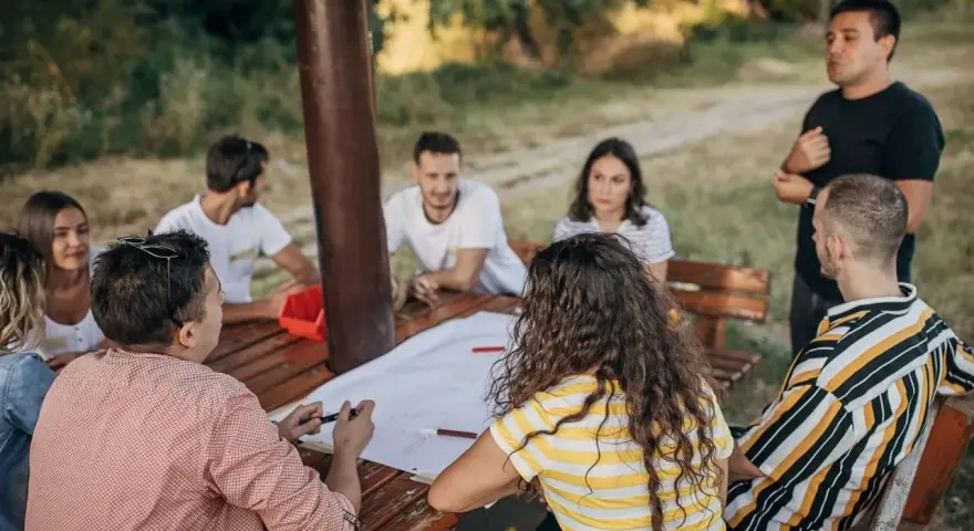 Un groupe discute autour d'une table en bois lors d'une sortie team building en plein air.
