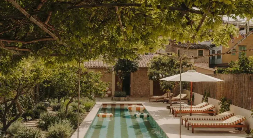 Piscina con galleggianti in un giardino rigoglioso, perfetto per idee piccoli giardini con piscina. Lettini e ombrellone invitano al relax.