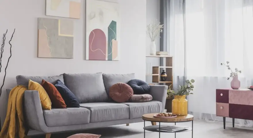 Divano grigio scuro con abbinamenti cuscini colorati e una coperta gialla. Tre quadri astratti decorano la parete.