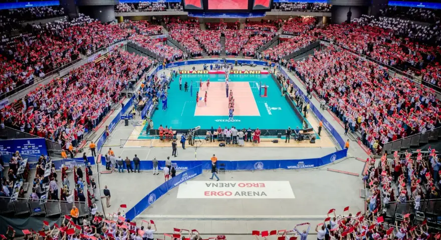 Widownia Ergo Areny, wypełniona kibicami z flagami Polski, dopingująca mecz siatkówki. Ogromna pojemność hali robi wrażenie.