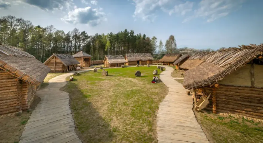 Drewniana osada średniowieczna Sławutowo z chatami krytymi strzechą, kamieniami i ścieżkami.